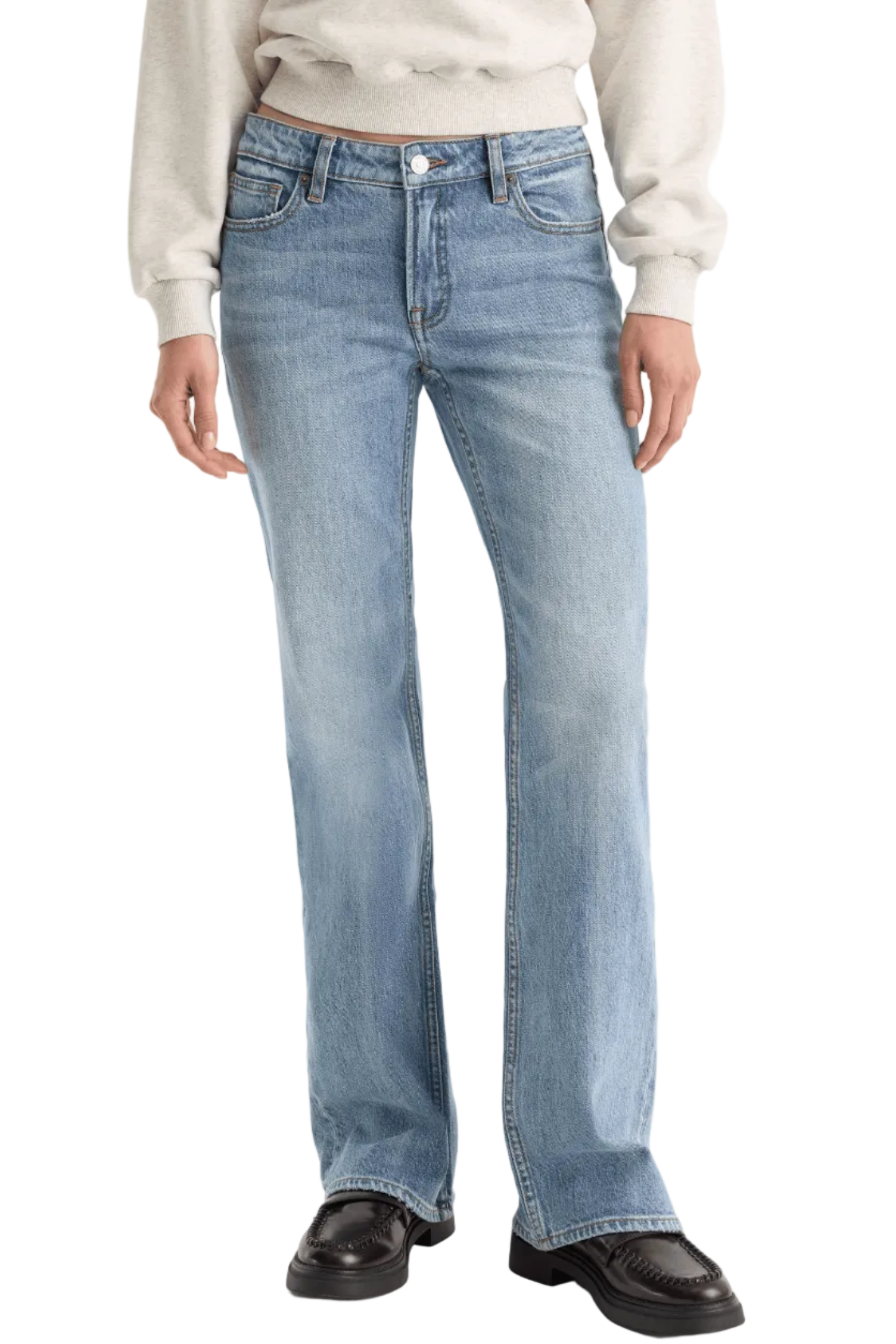 A person wearing light-wash blue jeans with a straight-to-medium leg fit, paired with a cream sweatshirt and dark brown leather loafers, shown from the waist down against a light gray studio background.